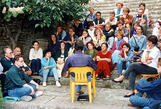 Participants gather around a speaker seated on the stone steps outside.