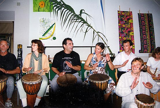 Participants play hand drums together in an indoor workshop.