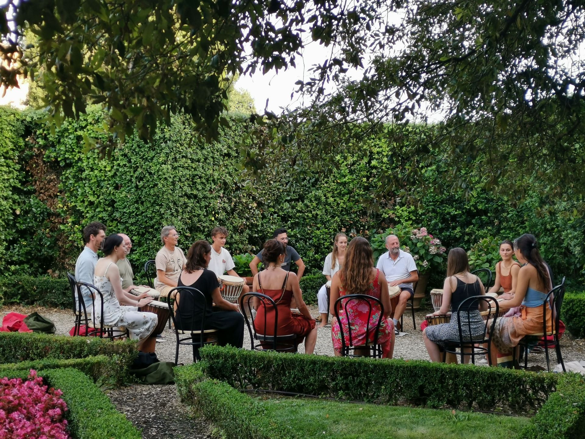 Participants play hand drums together in a circle in the garden.